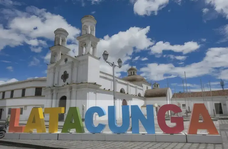 La imagen muestra el letrero de colores con el nombre de Latacunga, ubicado en la provincia de Cotopaxi, en Ecuador, con la fachada de un templo colonial al fondo (que parece ser la Catedral o una iglesia del centro histórico de la ciudad) Estrategia digital